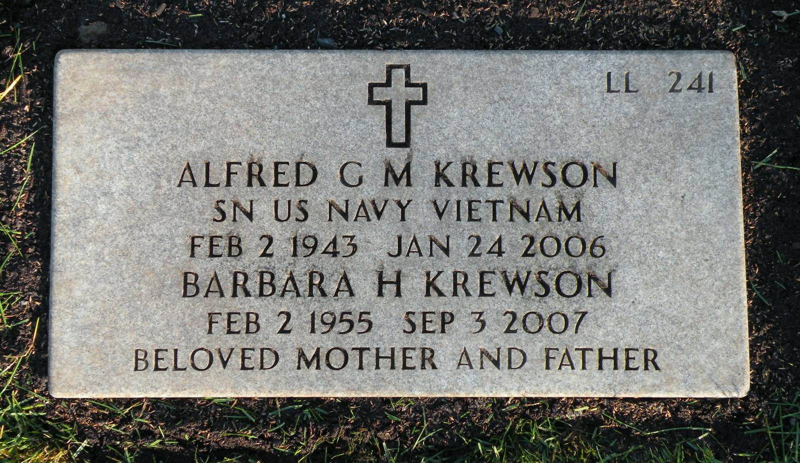 A flat granite grave marker set level with mown grass, incised with a Latin cross at the top and 'LL 241' in the upper right corner. The inscription reads: ALFRED G M KREWSON, SN US NAVY VIETNAM, FEB 2 1943, JAN 24 2006; BARBARA H KREWSON, FEB 2 1955, SEP 3 2007; BELOVED MOTHER AND FATHER.