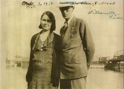 A sepia snapshot of a couple on a waterfront: a tall man in a pale wide-brimmed hat and a double-breasted suit, a young woman beside him in a patterned dress, piers and the far shore behind them. An inked caption across the sky reads 'Oct. 3, 1931' and 'Willamette River, Portland'.