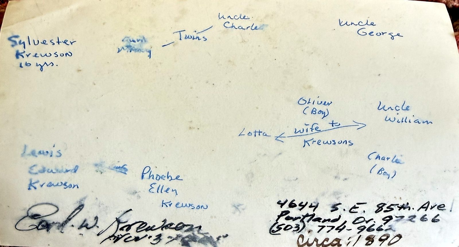 The blank reverse of an old photographic print, covered in blue ballpoint handwriting. Ten names are written spaced out across it rather than in a list: 'Sylvester Krewson 16 yrs.', 'aunt Mary' and 'Uncle Charles' joined by a line and labelled 'Twins', 'Uncle George', 'Oliver (Boy)', 'Uncle William', 'Lotta' with an arrow and the words 'wife to Krewsons', 'Charlie (Boy)', 'Lewis Edward Krewson' and 'Phoebe Ellen Krewson'. At the foot, a signature — Earl W. Krewson — with 'Nov 3', an address, '4644 S.E. 85th Ave. Portland, Or. 97266', a telephone number, and in a different pen, 'circa 1890'.